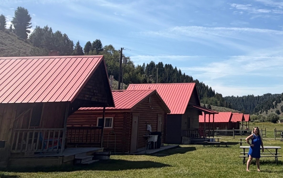 Megan standing among red-roof cabins in a grassy mountain valley
