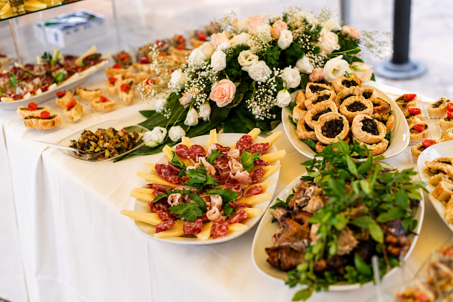 A catered event spread with charcuterie, pastries, appetizers, and a floral centerpiece