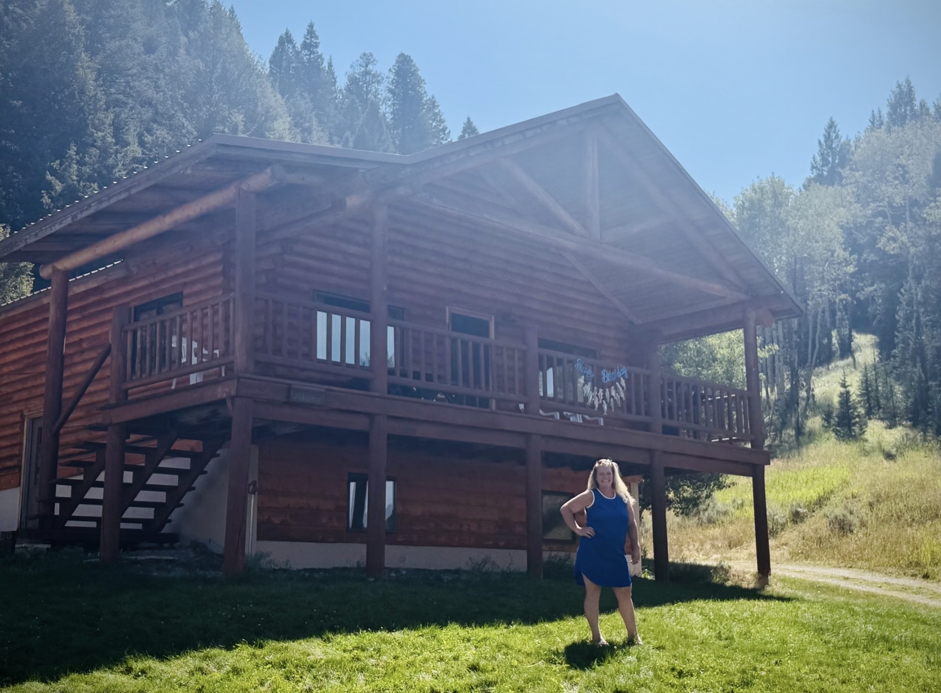 Megan standing in front of a large mountain cabin surrounded by trees